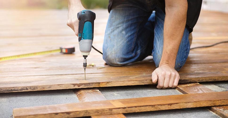 Man with blue drill installing a new deck in his backyard